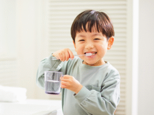 Happy child brushing teeth and holding a cup of water, showing how brushing can be a fun daily routine for kids.