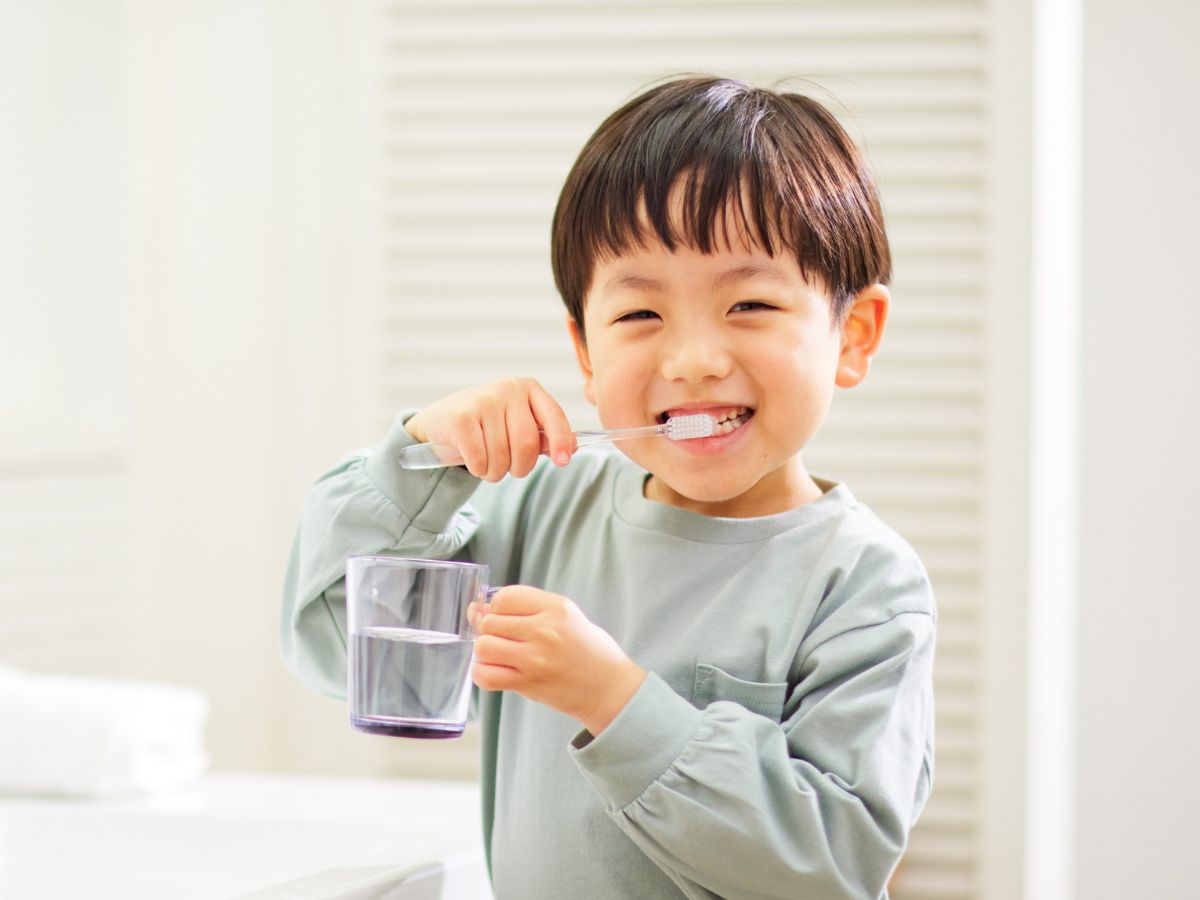 Happy child brushing teeth and holding a cup of water, showing how brushing can be a fun daily routine for kids.