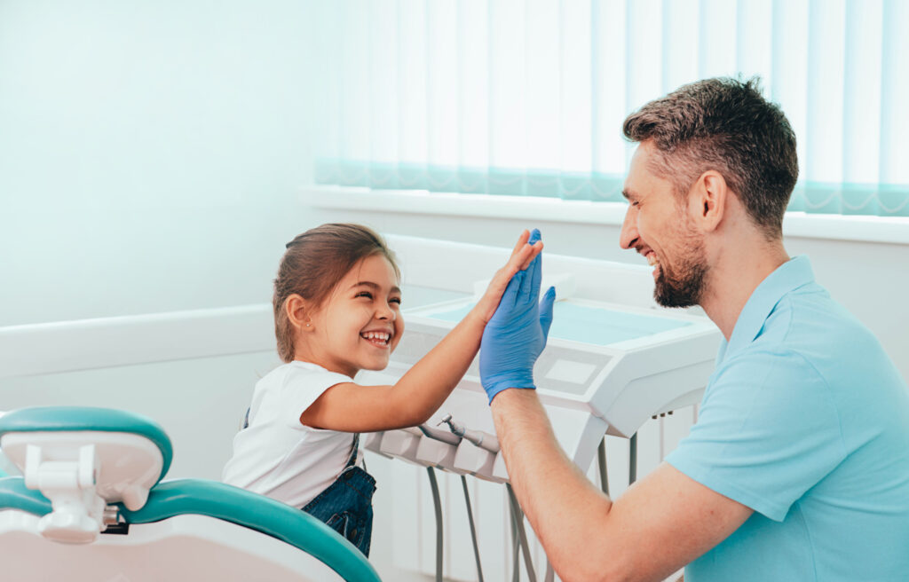 A dentist and a young child sharing a high five in a dental clinic.